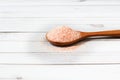 Fine pink Himalayan salt in wooden spoon on a white wooden background
