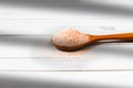 Fine pink Himalayan salt in wooden spoon on a white wooden background