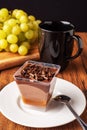 Finest chocolate dessert with chocolate chunks in focus, black cup with tea and fresh green grapes out of focus, Black background