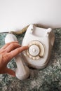 A finger dials a number on an old analog white Soviet telephone