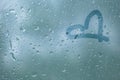 Finger-drawing a love symbol of a heart shape on a translucent sweated glass. raindrops of spring rain on the window close-up.