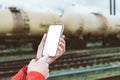 Finger in front of a Mockup of a phone in a man`s hand. Against the background of railway cars with oil products tanks. close-up