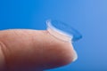 Finger holding contact lens over blue Royalty Free Stock Photo