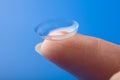 Finger holding contact lens over blue background Royalty Free Stock Photo