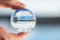 Finger holding a crystal or glass ball, winter landscape reflection, snow and trees with blue sky Royalty Free Stock Photo