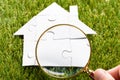 Finger Holding Magnifying Glass Over Puzzle House