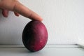 FInger holding a Painted Easter Boiled Egg on a White Wall