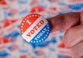 Finger with I Voted Today sticker in front of background created from many election voting badges