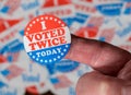 Finger with I Voted Twice sticker in front of many election voting badges to illustrate voter fraud Royalty Free Stock Photo