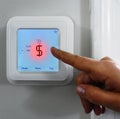 Finger pointing to a dollar sign in red on a smart thermostat -- heating and cooling cost concept