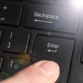 A finger pressing the `Enter` key on the black keyboard