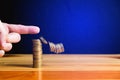 Finger pushing a column of coins on wooden table with black wall Royalty Free Stock Photo
