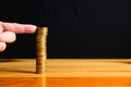 Finger pushing a column of coins on wooden table with black wall Royalty Free Stock Photo