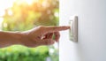 Finger activating a light switch on a white wall with sunlit green leaves in background Royalty Free Stock Photo