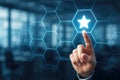 Finger touching a glowing star icon within a blue hexagonal grid on a blurred office background image Royalty Free Stock Photo