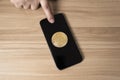 Finger touching the smartphone and bitcoin on wooden table concept cryptocurrency exchan