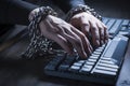 Fingers confined by cuffs engage keyboard, delving into the world of cybercrime