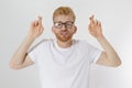 Fingers crossed, make a wish concept. Young redheaded guy with red beard cross finger for good luck. Hand sign, gesture for dreams