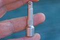 Fingers on the hand hold one small gray metal adapter for a screwdriver