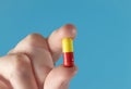 Fingers holding up a yellow and red medicine capsule. Extreme macro closeup with a blue background Royalty Free Stock Photo