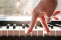 Fingers press the keys of the piano, as if legs were walking, in natural light from the window.