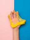 The fingers of the right hand break a yellow slime on a pink and blue background. Royalty Free Stock Photo