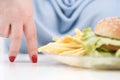 Fingers of a young lush fat woman in casual blue clothes on a white background, the choice between healthy food and fast Royalty Free Stock Photo