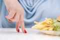 Fingers of a young lush fat woman in casual blue clothes on a white background, the choice between healthy food and fast Royalty Free Stock Photo