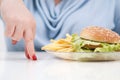 Fingers of a young lush fat woman in casual blue clothes on a white background, the choice between healthy food and fast Royalty Free Stock Photo