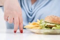 Fingers of a young lush fat woman in casual blue clothes on a white background, the choice between healthy food and fast Royalty Free Stock Photo