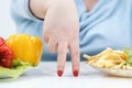 Fingers of a young lush fat woman in casual blue clothes on a white background, the choice between healthy food and fast Royalty Free Stock Photo