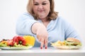 Fingers of a young lush fat woman in casual blue clothes on a white background, the choice between healthy food and fast Royalty Free Stock Photo