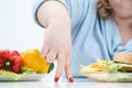 Fingers of a young lush fat woman in casual blue clothes on a white background, the choice between healthy food and fast Royalty Free Stock Photo
