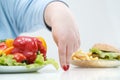 Fingers of a young lush fat woman in casual blue clothes on a white background, the choice between healthy food and fast Royalty Free Stock Photo