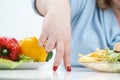 Fingers of a young lush fat woman in casual blue clothes on a white background, the choice between healthy food and fast Royalty Free Stock Photo