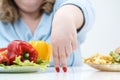 Fingers of a young lush fat woman in casual blue clothes on a white background, the choice between healthy food and fast Royalty Free Stock Photo