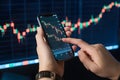Fingertips grip smartphone displaying cryptocurrency candlestick chart