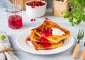 Finnish pancake pannukakku with redcurrant jam and sour cream or whipped cream on a white ceramic plate on a light wooden Royalty Free Stock Photo