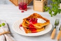 Finnish pancake pannukakku with redcurrant jam and sour cream or whipped cream on a white ceramic plate on a light wooden Royalty Free Stock Photo