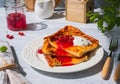 Finnish pancake pannukakku with redcurrant jam and sour cream or whipped cream on a white ceramic plate on a light wooden Royalty Free Stock Photo