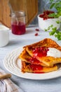 Finnish pancake pannukakku with redcurrant jam and sour cream or whipped cream on a white ceramic plate on a light wooden Royalty Free Stock Photo