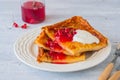 Finnish pancake pannukakku with redcurrant jam and sour cream or whipped cream on a white ceramic plate on a light wooden Royalty Free Stock Photo