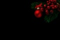 Fir branches adorned with bunches of red berries, a red Christmas ball with a bow and a pine cone painted gold on a black Royalty Free Stock Photo