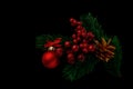 Fir branches adorned with bunches of red berries, a red Christmas ball with a bow and a pine cone painted gold on a black Royalty Free Stock Photo