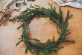 Fir branches circle, thread, berries, herbs on wooden table. Rustic Christmas wreath workshop. Authentic stylish still life.