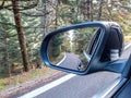 Fir forest and asphalt road in car rear side view mirror. Travel in the mountain Royalty Free Stock Photo