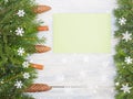 Fir tree branch with cones, cinnamon, green envelope, snowflake on white wooden background