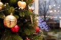 Fir tree branches decorated for Merry Christmas with red and golden ornaments, garland. Lights bokeh behind window, street Royalty Free Stock Photo