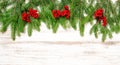 Fir tree twigs with red berries on bright wooden background