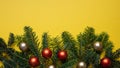 Fir twig fresh and christmas baubles against yellow color background